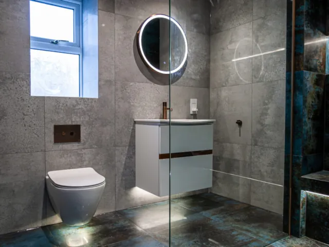 Grey tiled shower room with wall-hung toilet, floating vanity and round LED mirror