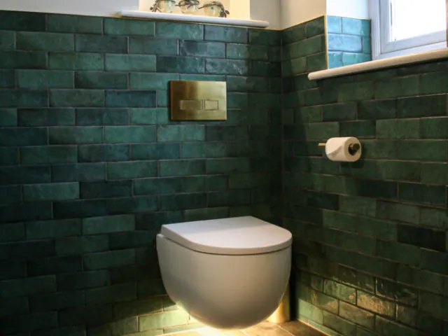 Cloakroom with green metro tiles, wall-hung toilet and brass flush plate