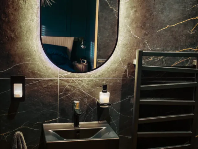 Dark marble-effect bathroom with backlit oval mirror and black basin