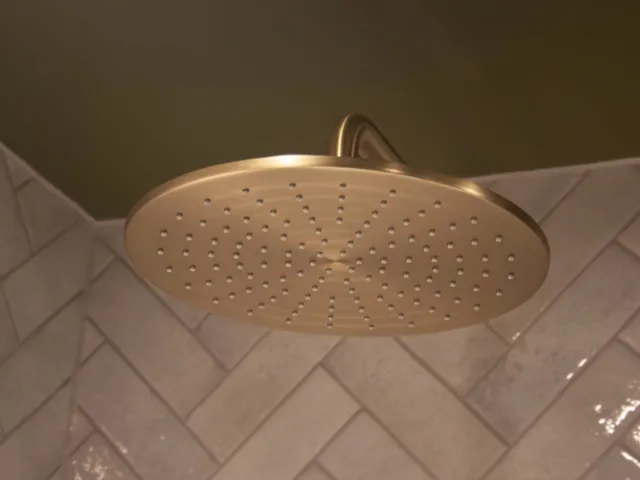 Brushed brass rain shower head against white herringbone tiles