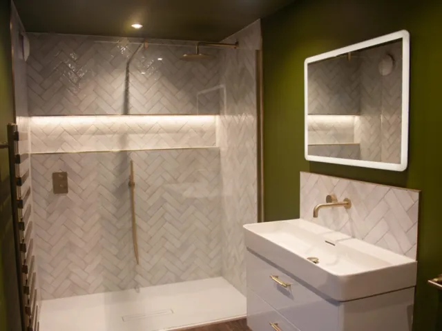 Walk-in shower with white herringbone tiles, brass fittings and a lit niche
