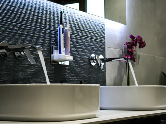 Twin vessel basins with wall-mounted taps against dark textured tiles
