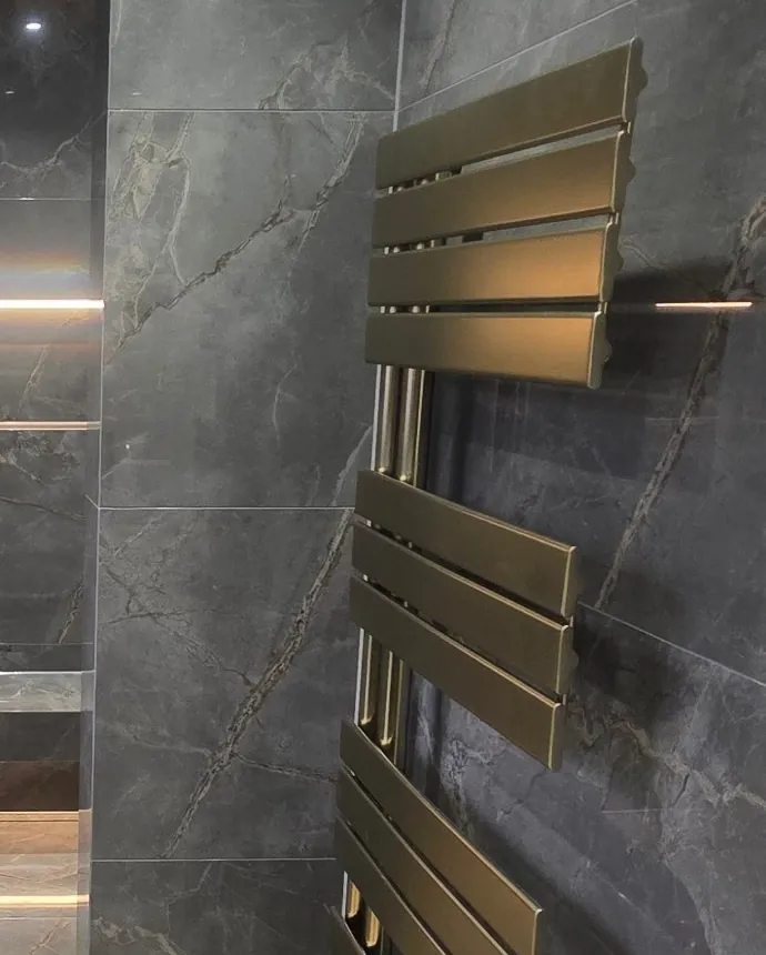 Brushed brass towel radiator on dark marble-effect tiles