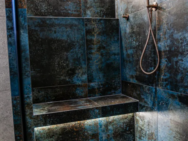 Walk-in shower with metallic blue tiles, built-in bench and copper fittings